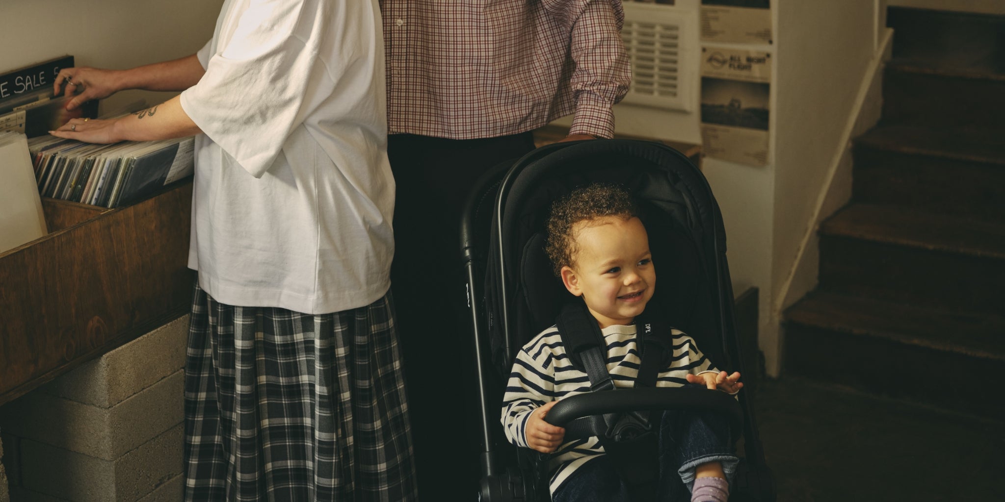 Baby sat in stroller while mum and day look for records in a record store